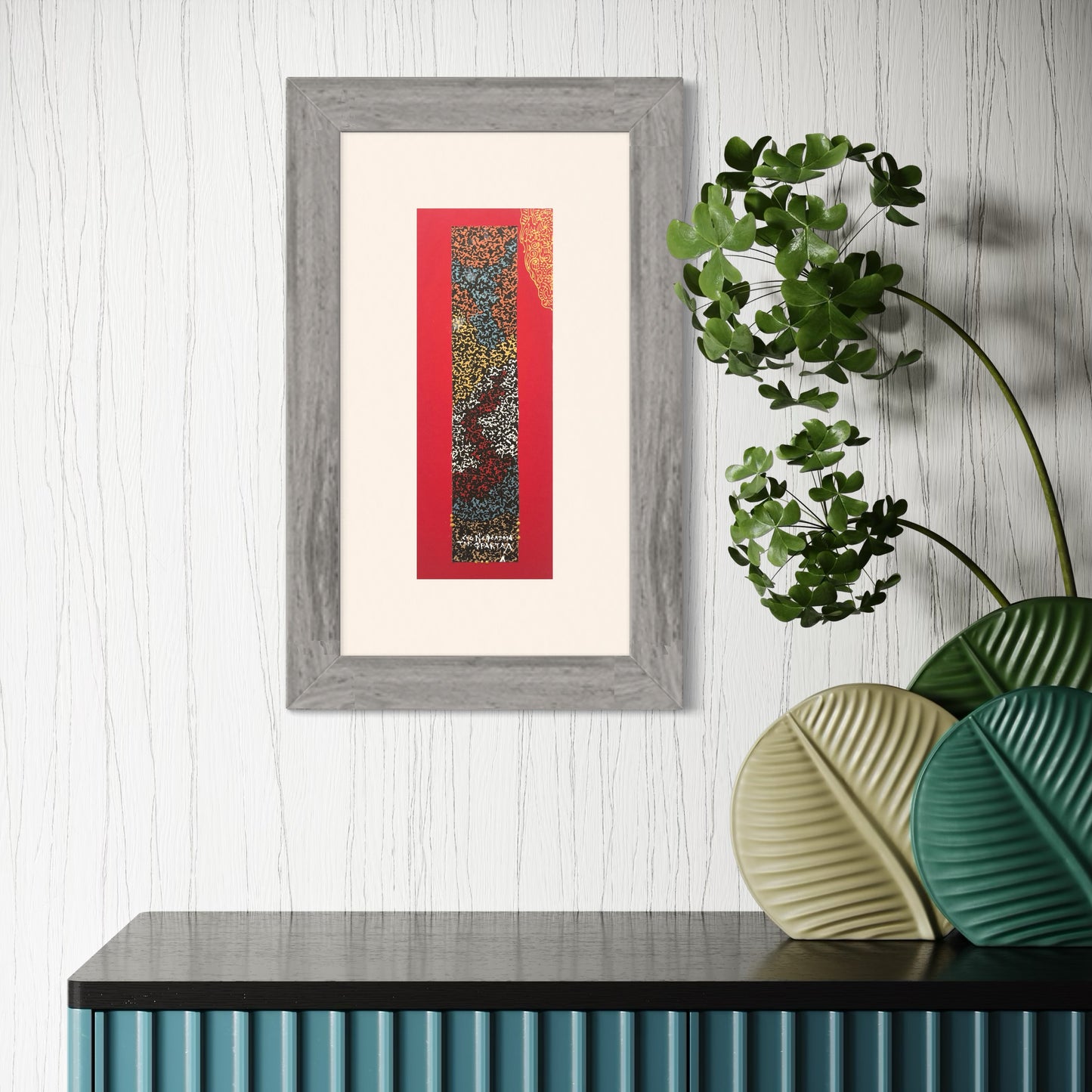 A framed abstract drawing mounted on red card, displayed on a wall above a cabinet, with a gray frame and a mix of red, gold, and white colors.