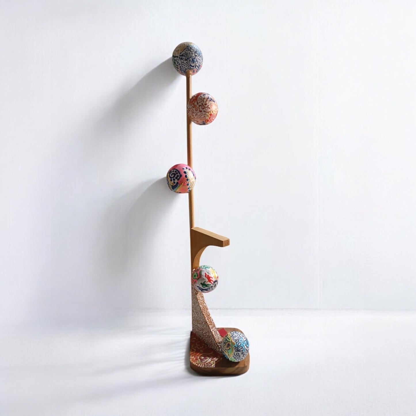 A mixed media sculpture consisting of a wooden structure with multiple colorful spherical attachments, standing upright against a white background.