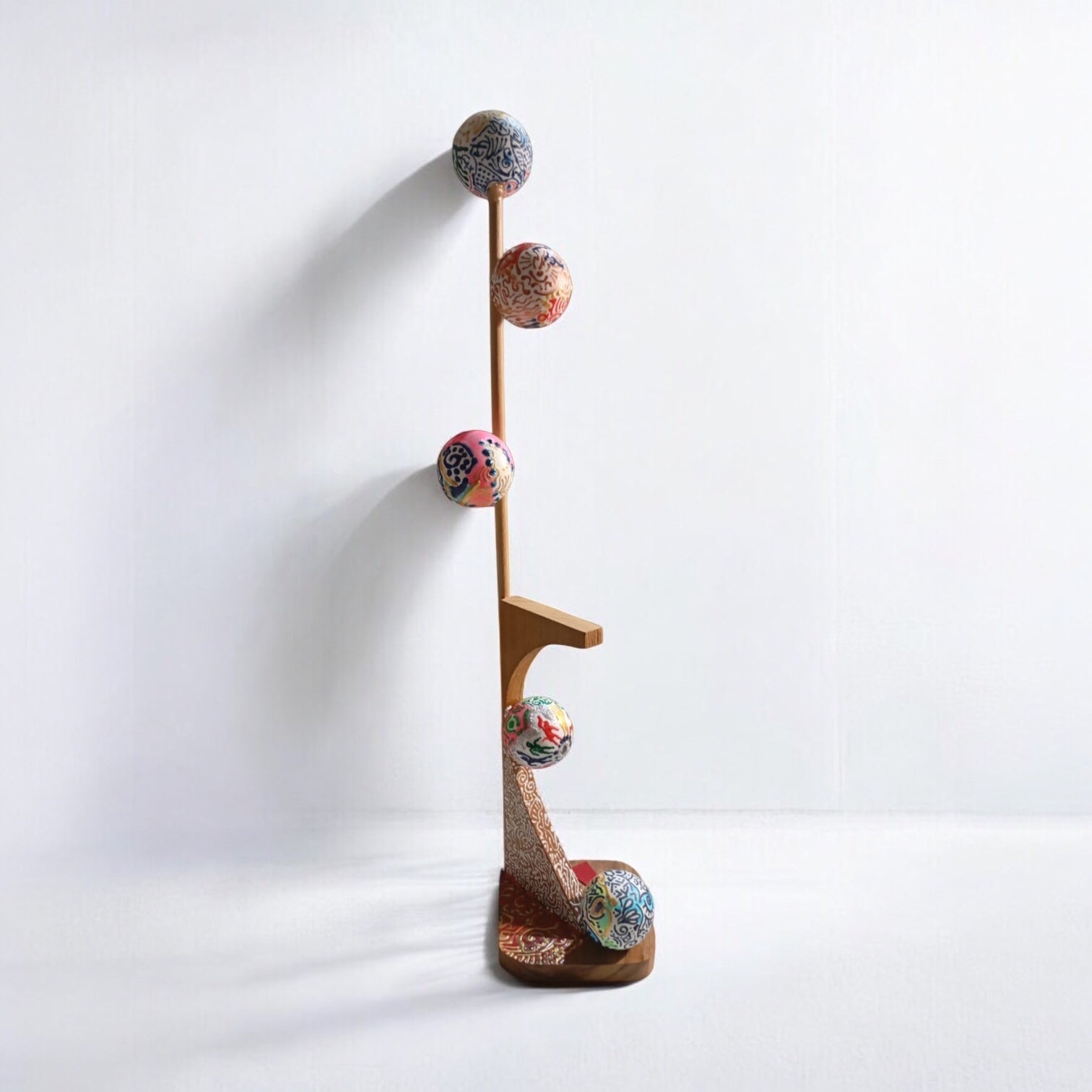 A mixed media sculpture consisting of a wooden structure with multiple colorful spherical attachments, standing upright against a white background.