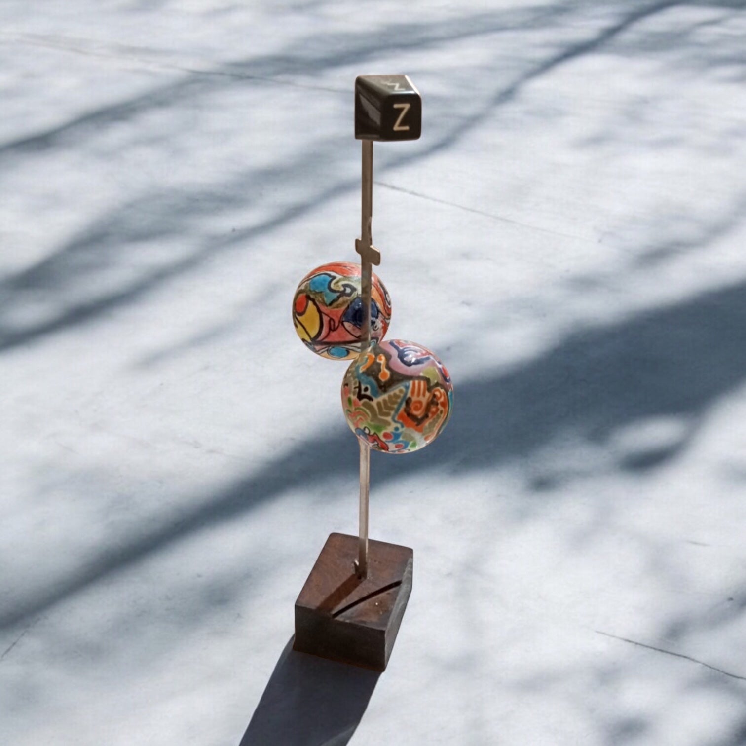 A sculpture featuring two multicolored spherical objects mounted on a vertical rod, with a small square base, placed on a snowy surface.