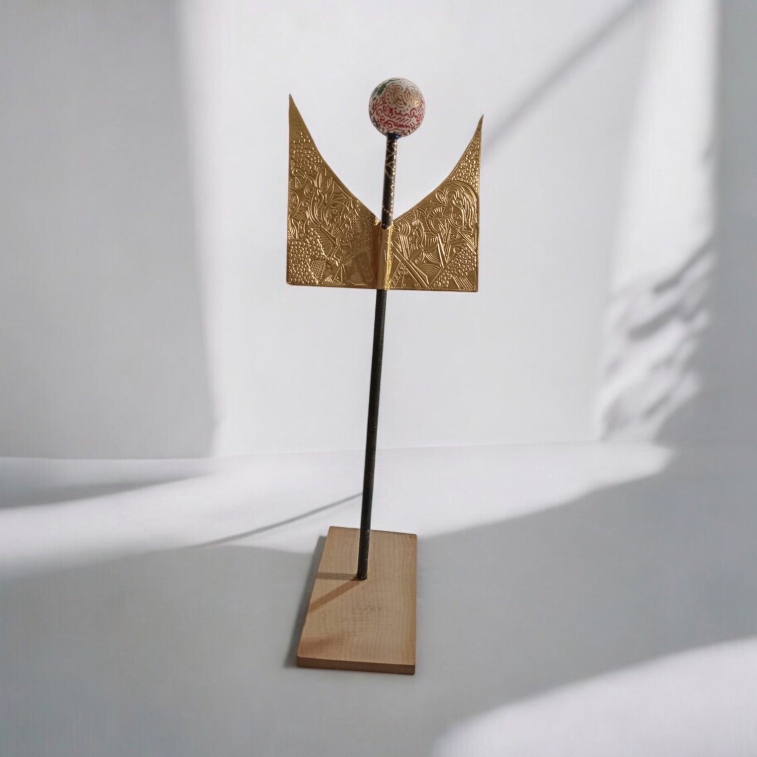 A mixed media sculpture with bronze elements, recycled materials, and wood displayed on a stand.