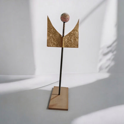 A mixed media sculpture with bronze elements, recycled materials, and wood displayed on a stand.