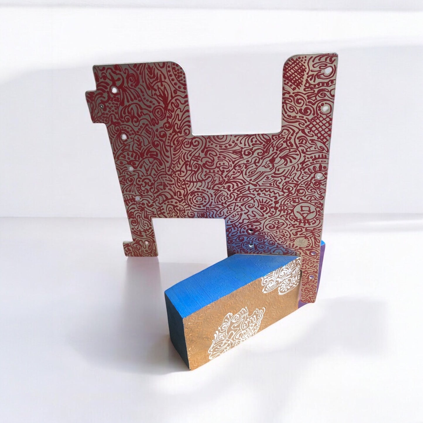 A metal and wood sculpture of an abstract flat bull with intricate patterns in red and blue on a metal background.
